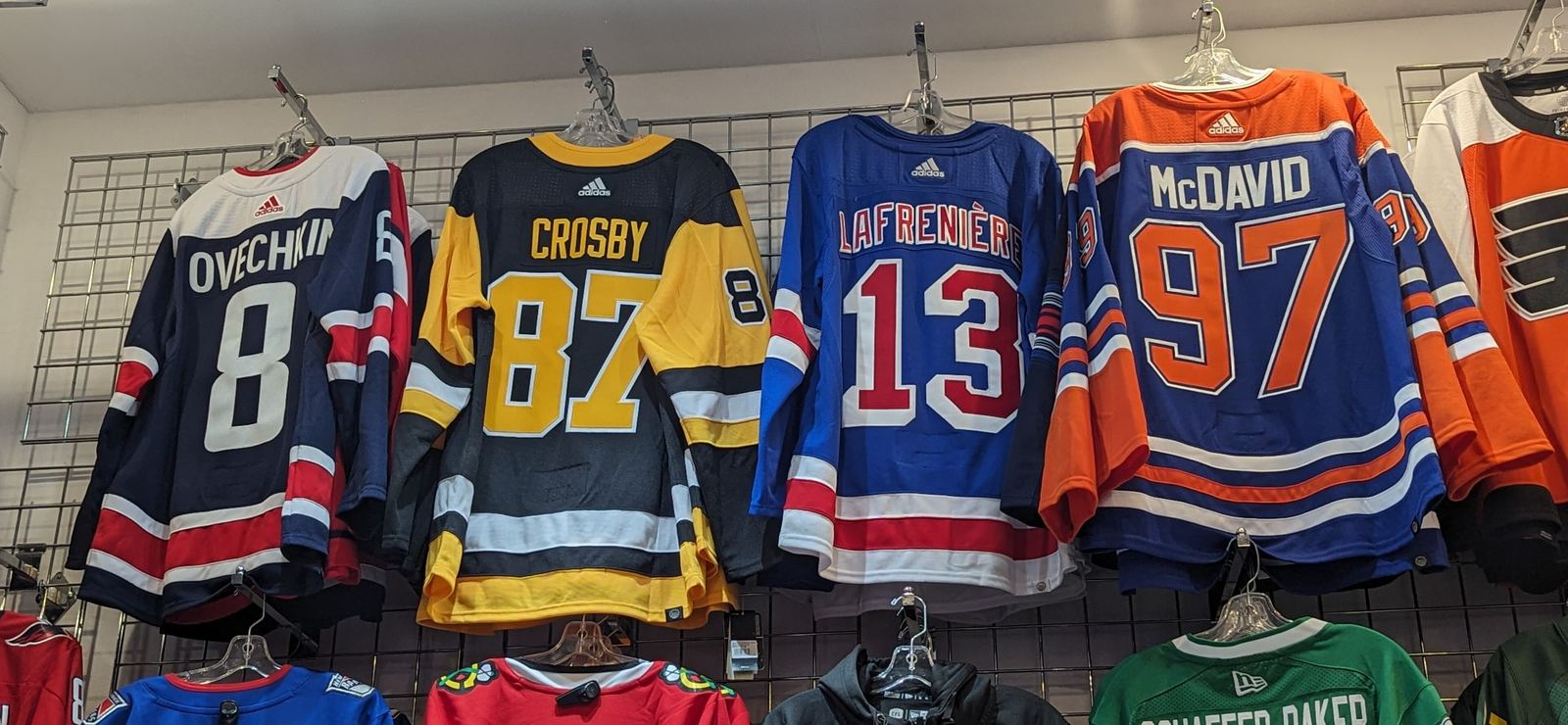 A McDavid number 97 Oilers jersey hanging on a retail rack beside Ovechkin, Crosby and Lafrenière jerseys.